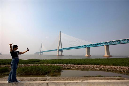 6月30日，一名女子在沪苏通长江公铁大桥南岸拍照。该桥于7月1日正式通车。横跨长江，两岸连接江苏省南通市和张家港市，为国内最大跨度斜拉桥，也是世界最大跨度公铁两用斜拉桥。泱波/中新社 图